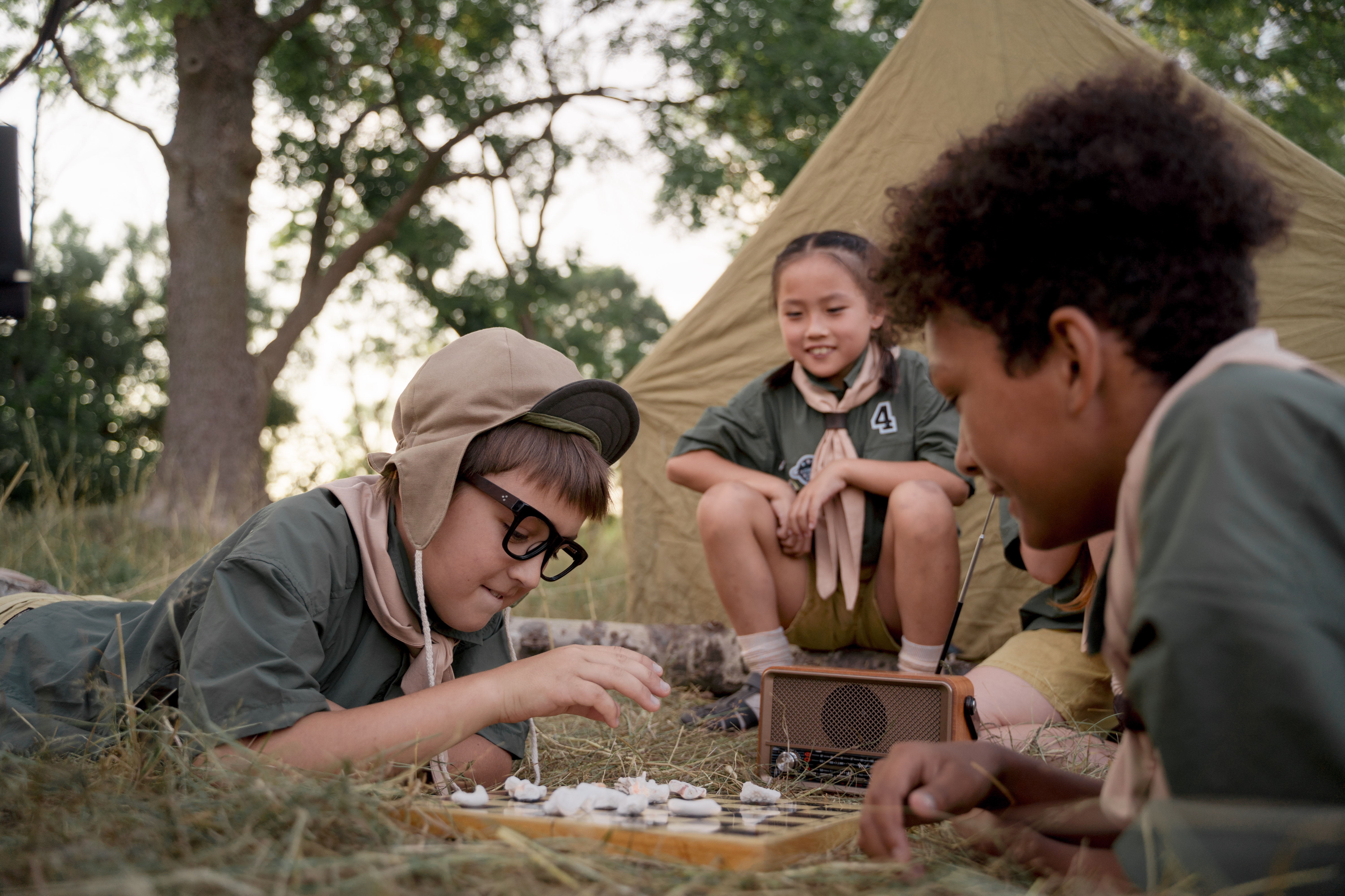 3 scouts children playing chess in front of their tent whilst camping
